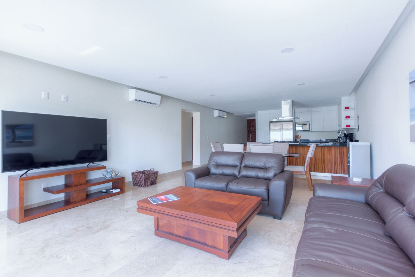 Een moderne woonkamer met een flatscreentelevisie, leren banken, een houten salontafel en een keuken op de achtergrond.
