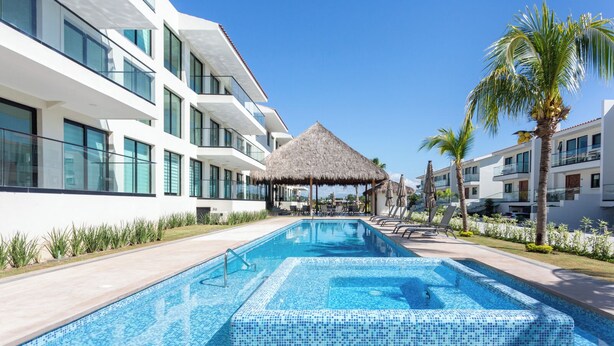 Un hotel moderno con piscina, pabellón de techo de paja y palmeras.