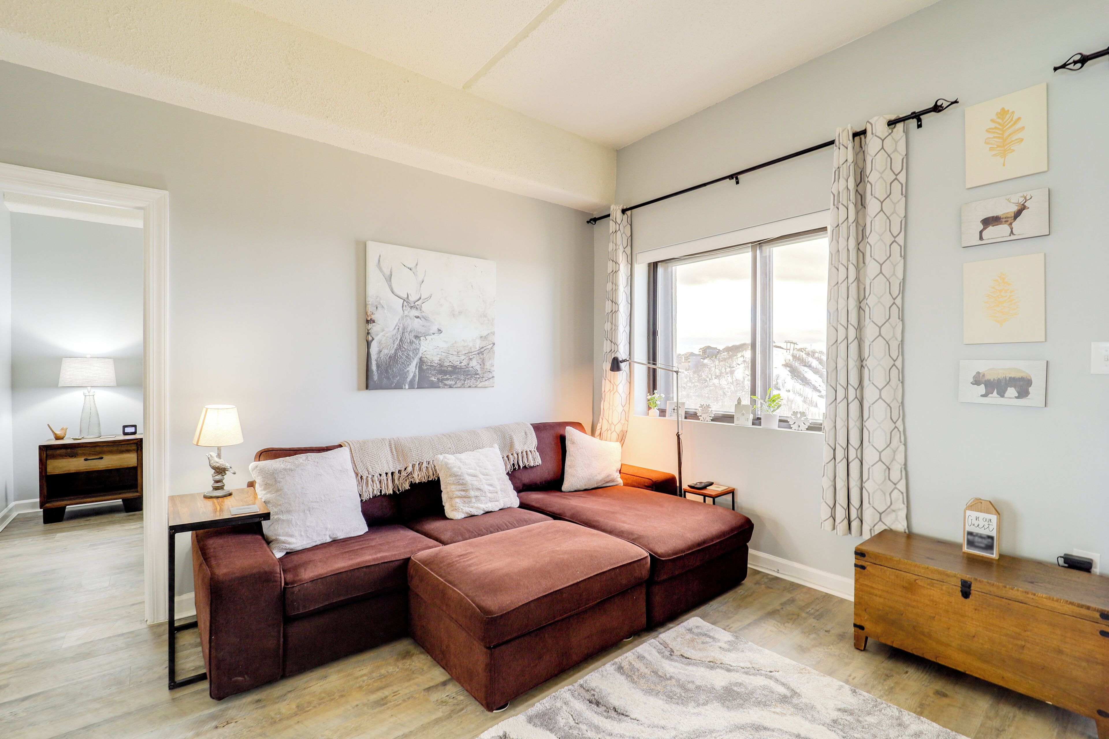 Una sala de estar moderna con un sofá seccional, una mesita de madera, una lámpara y un ventanal con cortinas.