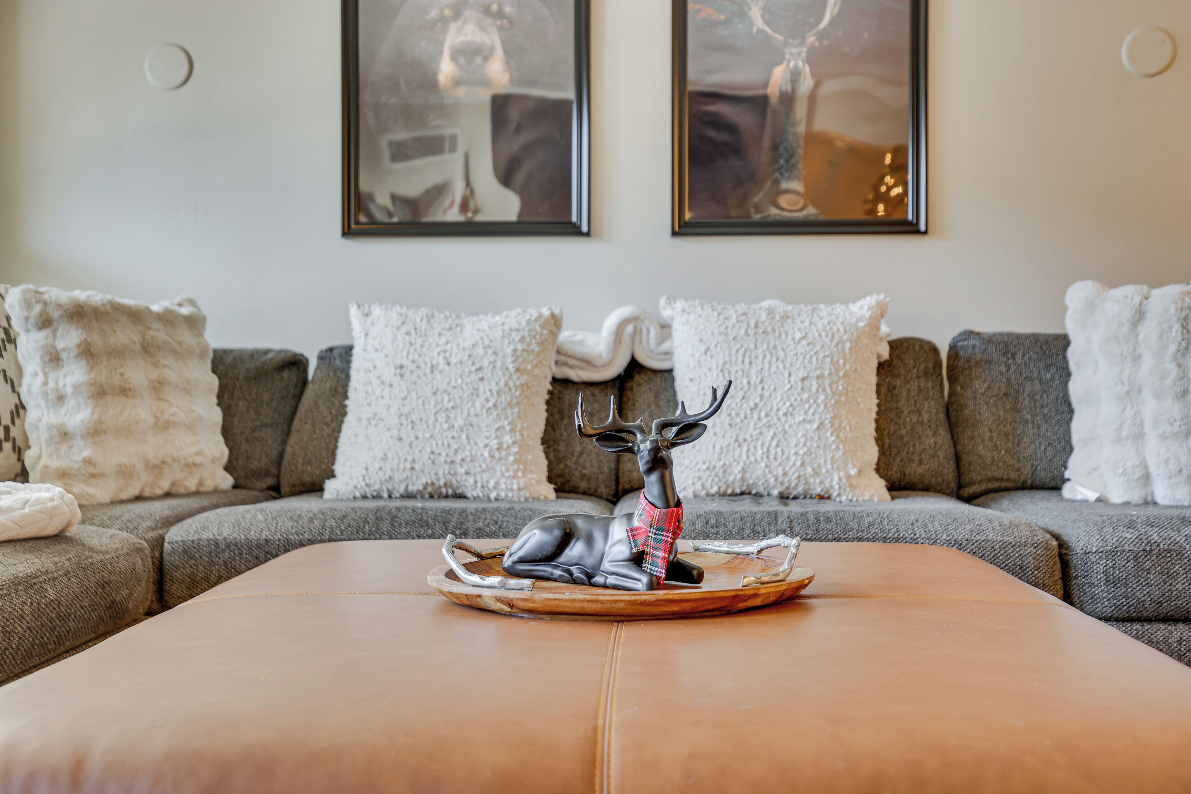 A modern living room with a grey sectional sofa, white pillows, and a wooden coffee table with a deer figurine.
