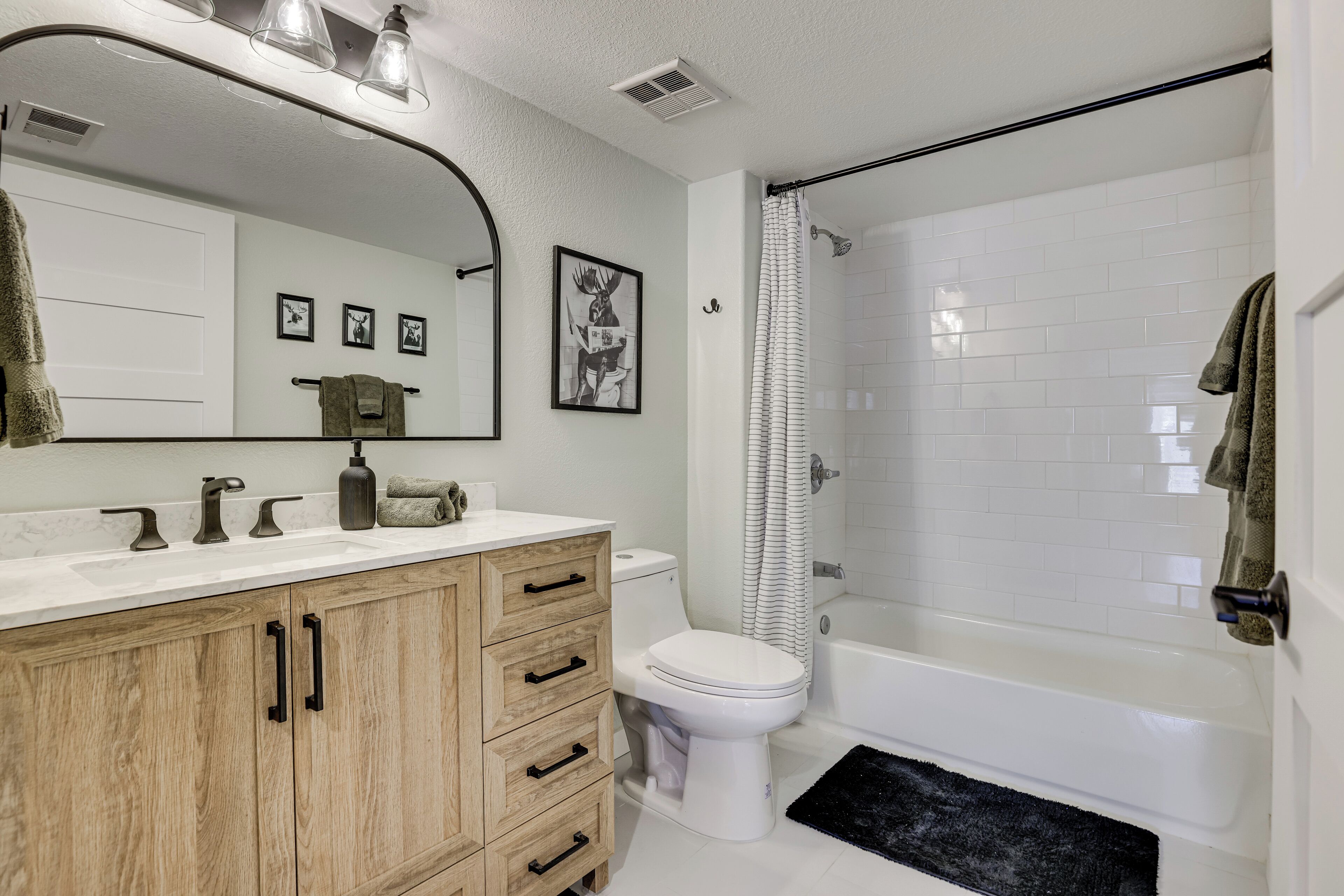 A bathroom with a wooden vanity, a white toilet, a bathtub, and a shower curtain.