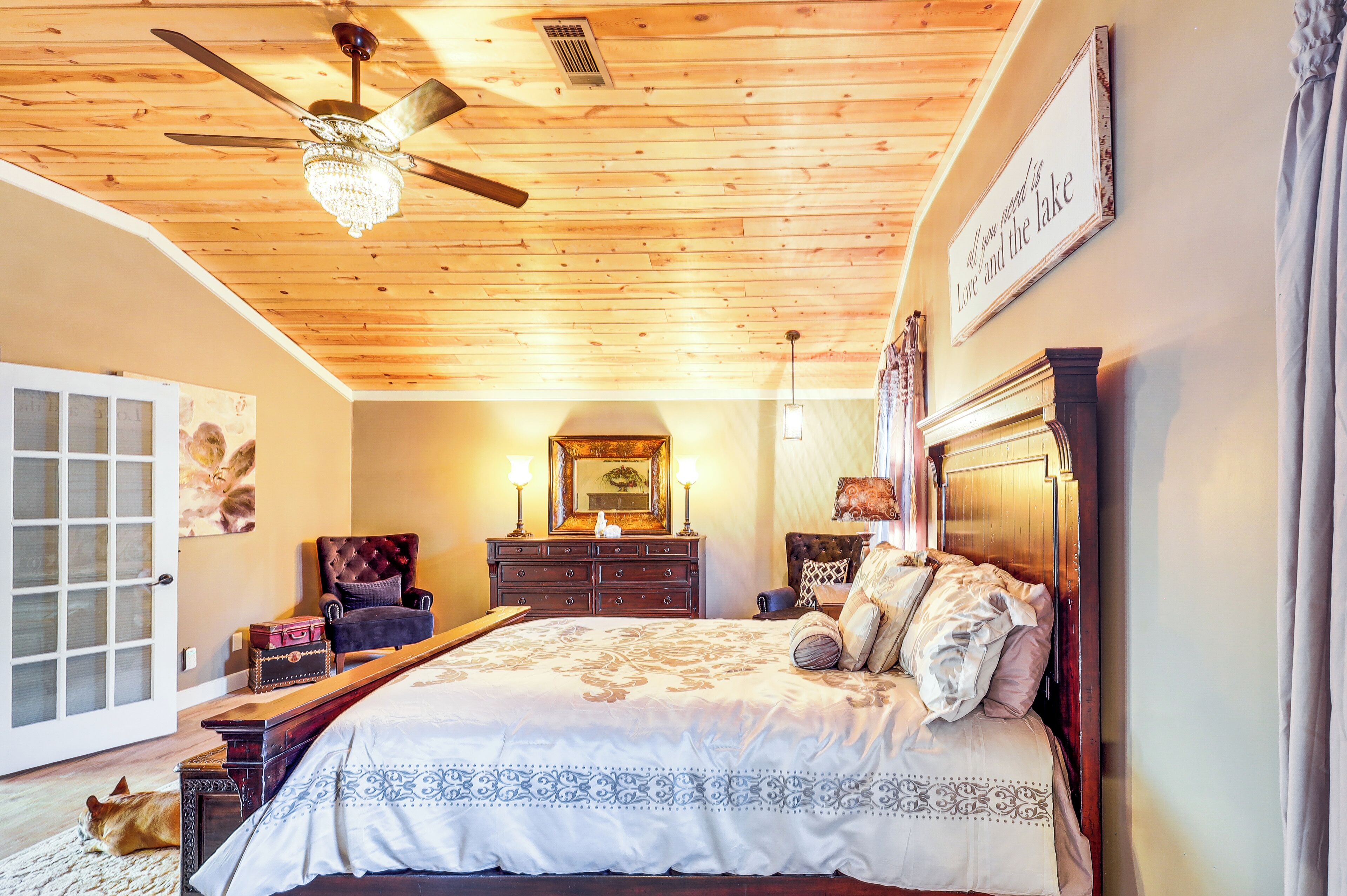 Une chambre avec un plafond en bois, un lit recouvert d’une couvre-lit à motifs floraux, une commode, un miroir et un lustre.