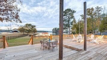 Une terrasse en bois avec des meubles d’extérieur, une vue sur un lac et un belvédère en arrière-plan.