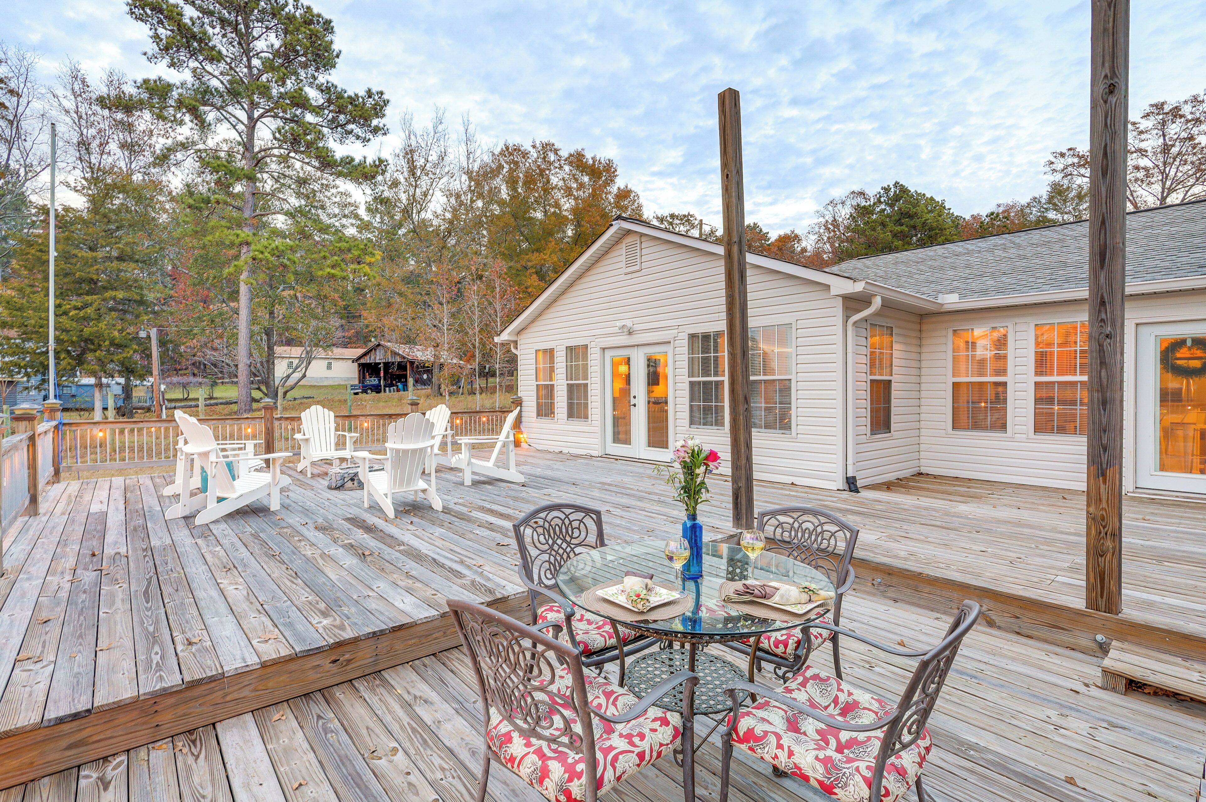 A wooden deck with outdoor furniture, a glass table, and a view of a white house in the background.