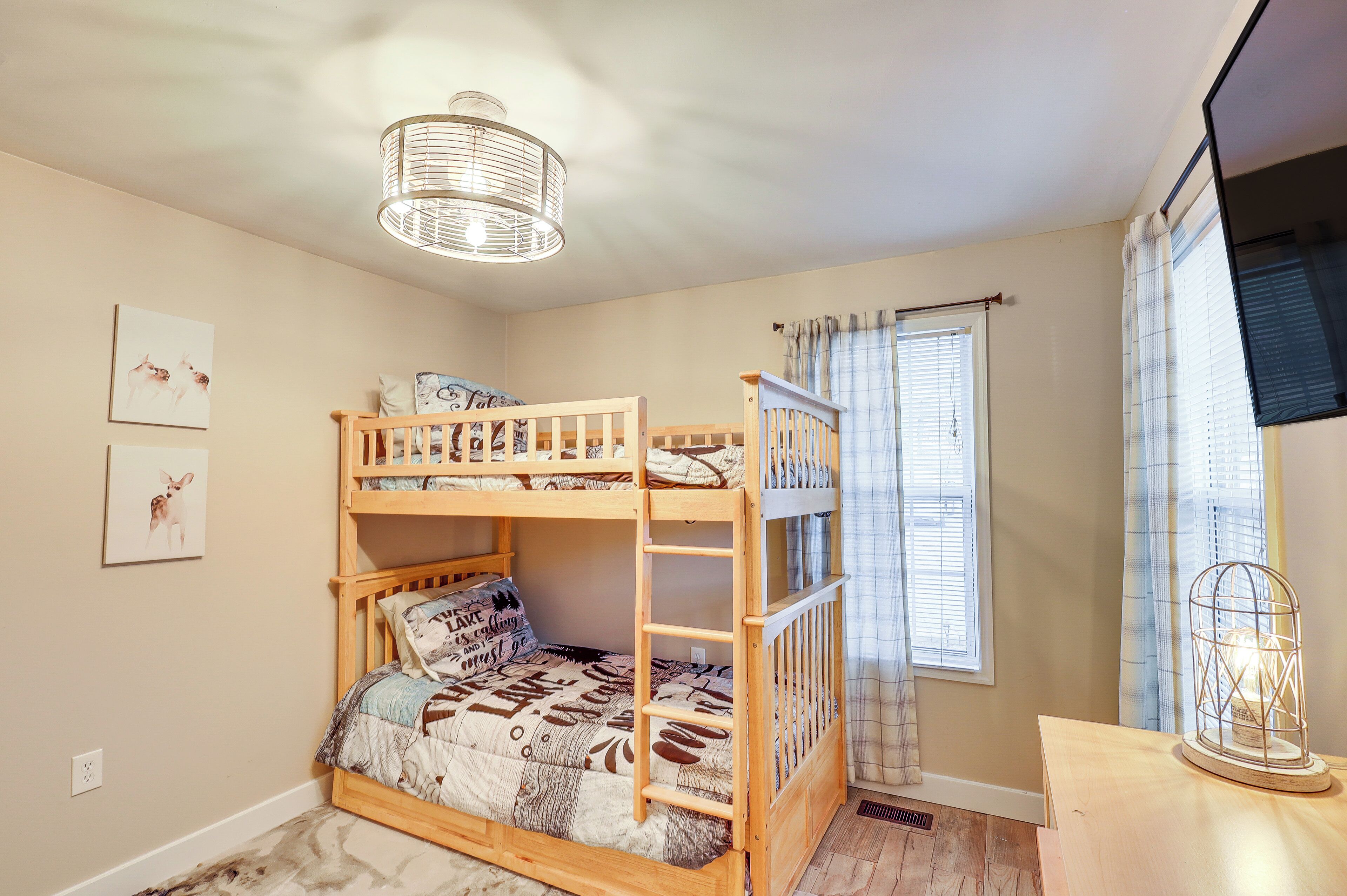 Una cama litera con escalera, un escritorio de madera, una lámpara y una ventana con cortinas.