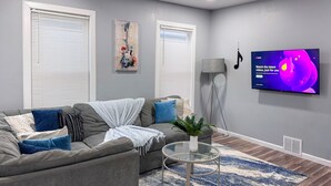 A modern living room with a grey sofa, a glass coffee table, and a blue patterned rug. - Rhythm & Blues Retreat near Syracuse University! (Syracuse)