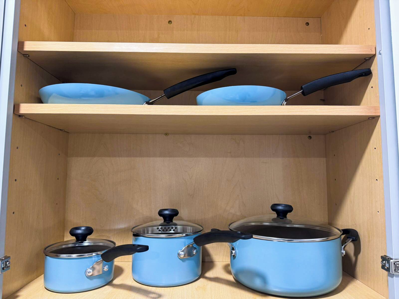 A kitchen cabinet with three pots and two frying pans.