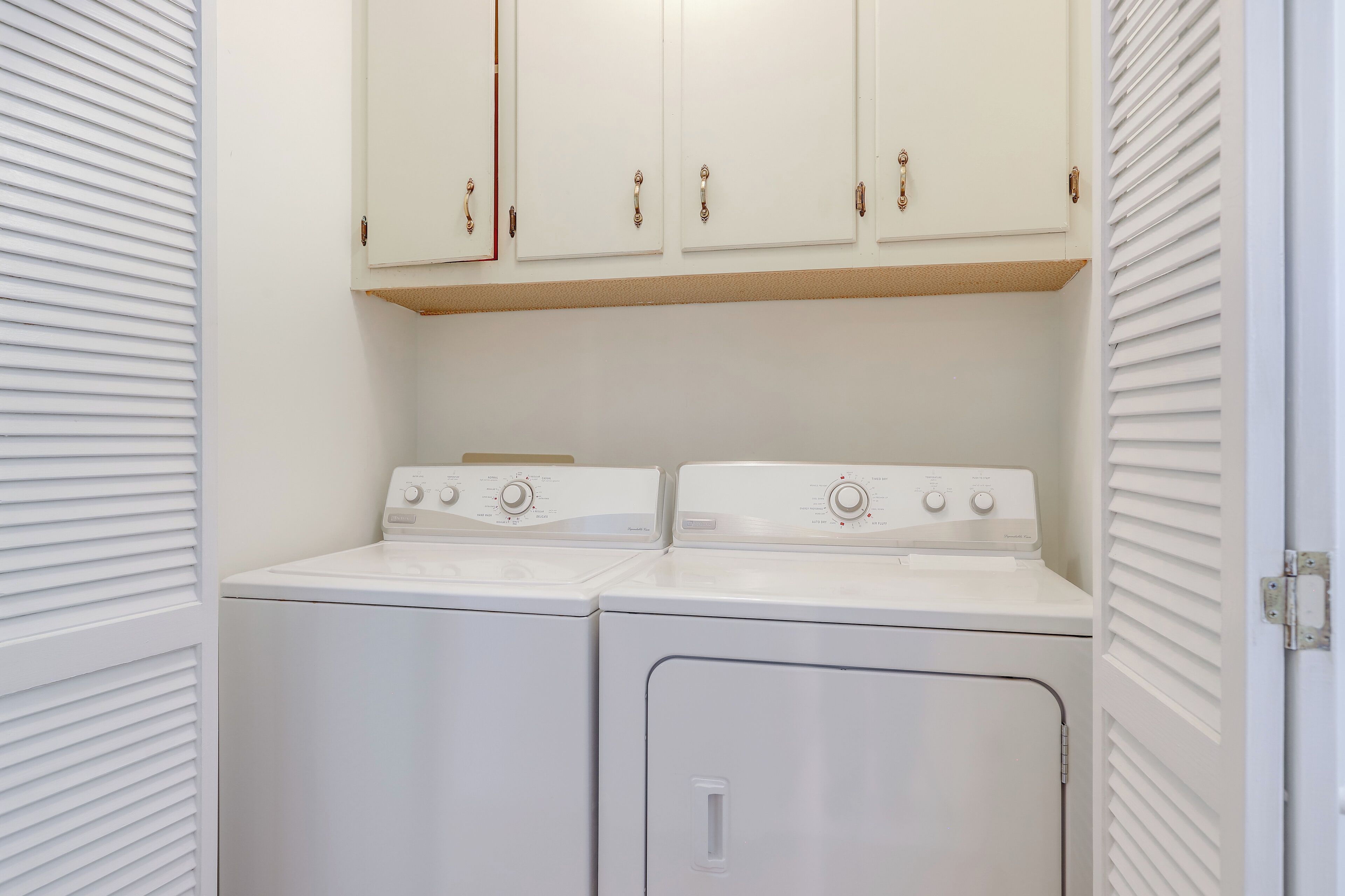 A laundry room with two white washers and dryers, wooden cabinets above, and a door with a metal handle.
