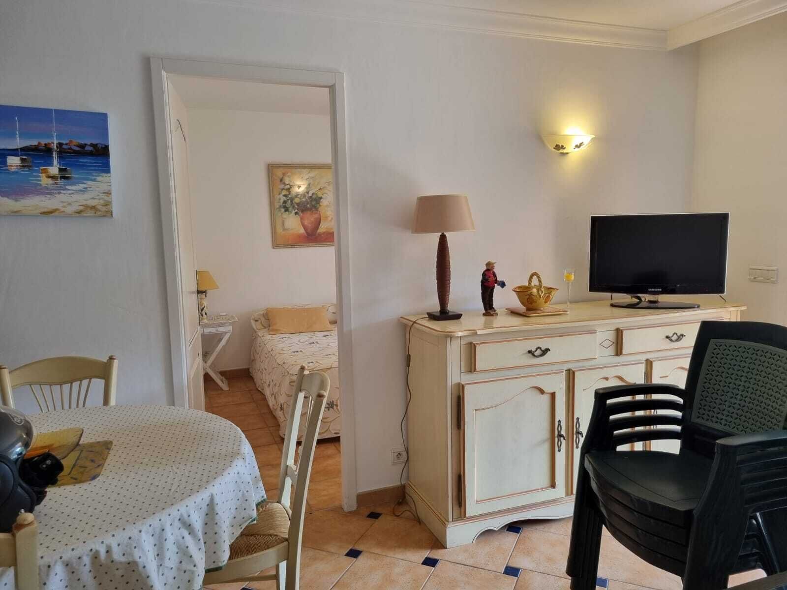 A room with a bed, a television, a dining table with chairs, and a small cabinet.