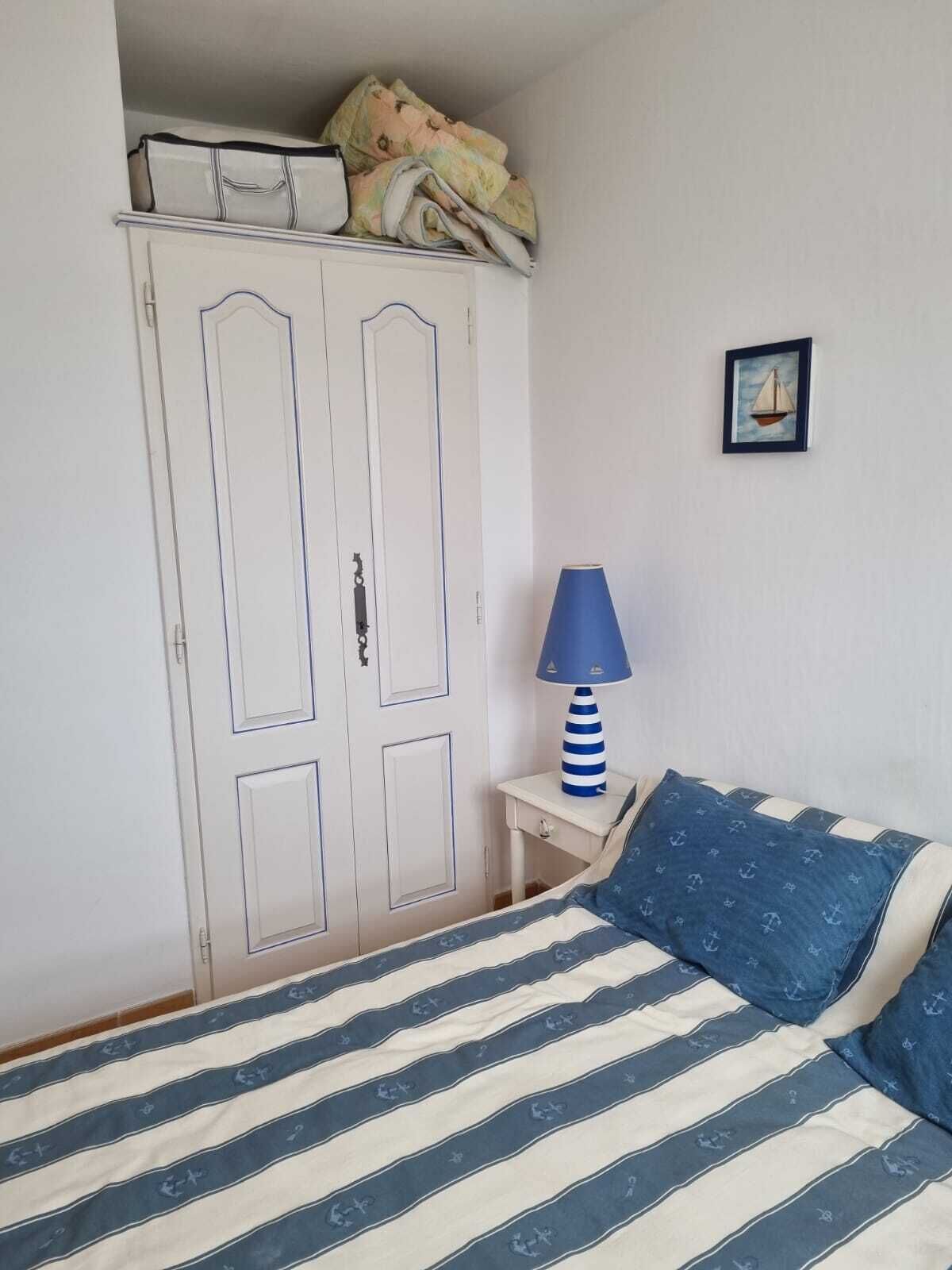 Una camera da letto con un letto, un armadio, un comodino con una lampada e un quadro appeso al muro.