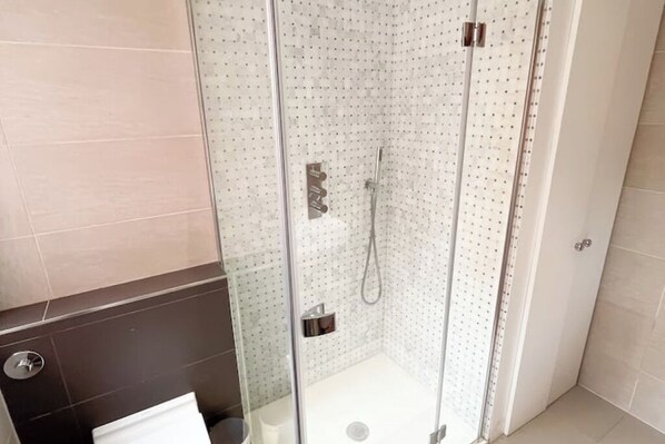 Cabina de ducha con paredes de vidrio, ducha de mano y panel de control en la pared.