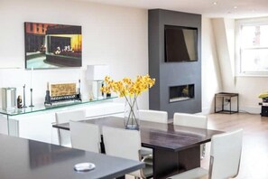 Un comedor moderno con una pared divisoria de vidrio, sillas blancas, una mesa oscura y un jarrón con flores amarillas.