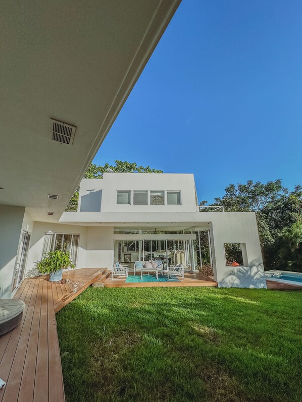 A modern two-story house with a patio, a pool, and a well-maintained lawn.