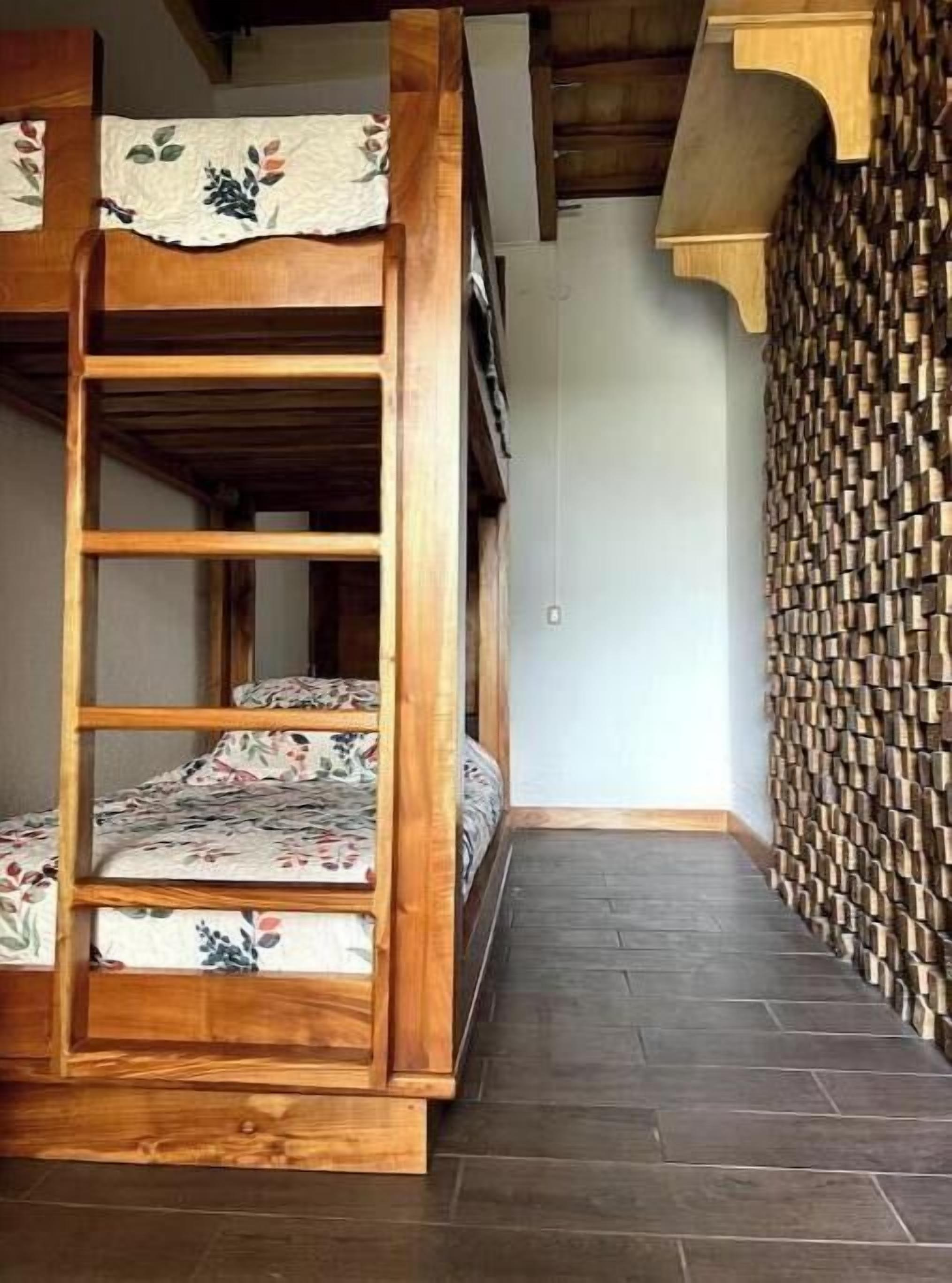Un lit superposé avec une literie à motifs floraux, une échelle en bois et un mur orné d’un motif géométrique.