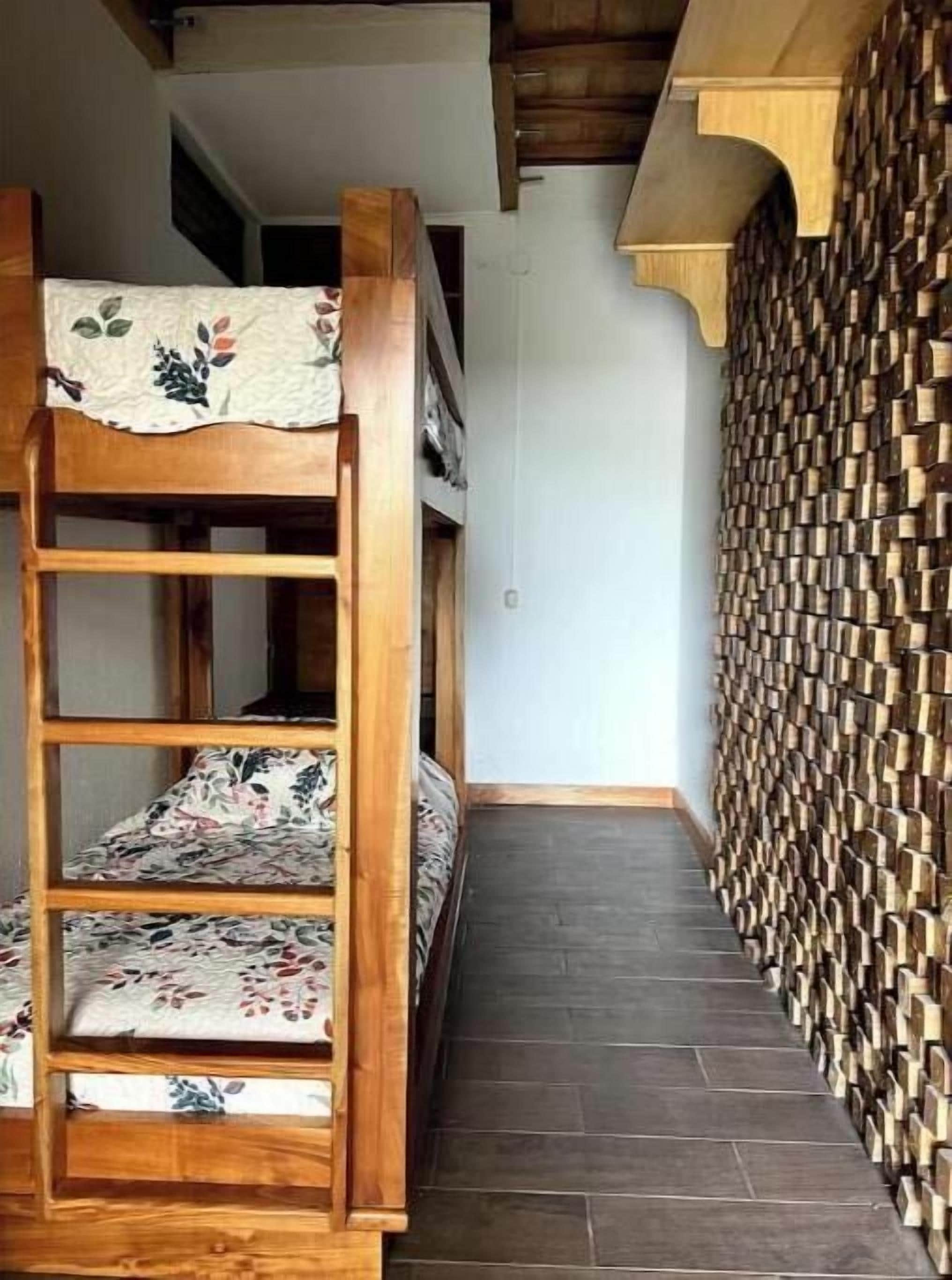 Un lit superposé avec une literie à motifs floraux, situé dans un couloir étroit avec un mur en bois et un sol carrelé.