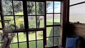 A room with large windows, a hammock, a chair, and a small table with a decorative item.