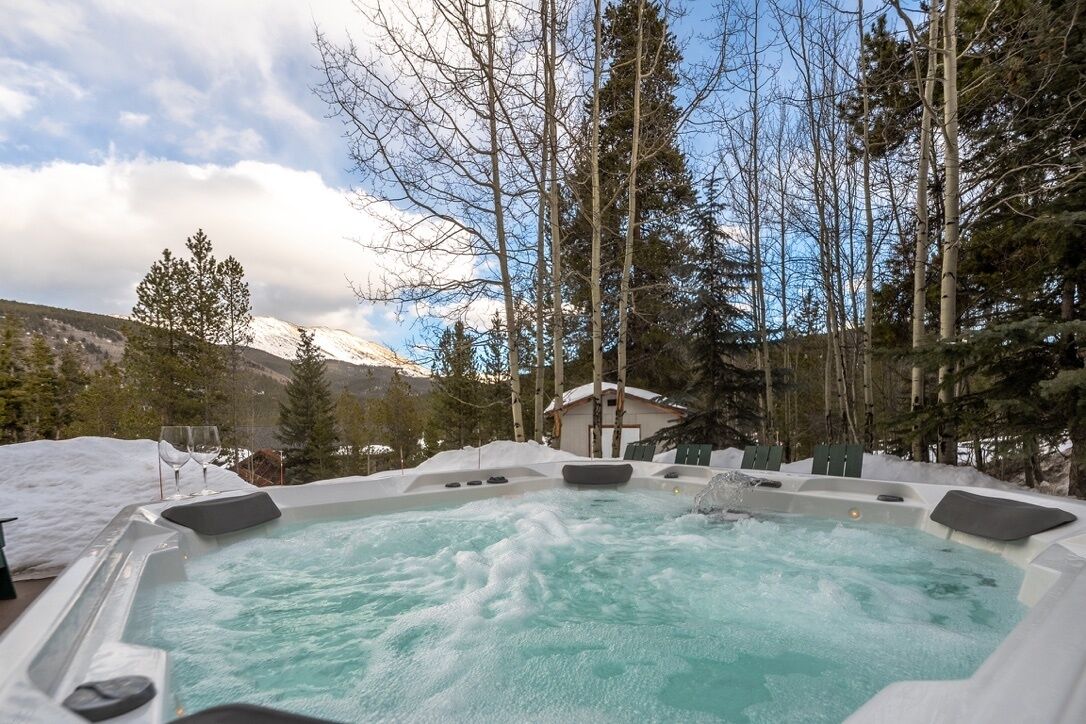 A hot tub surrounded by snow and trees, with a mountain in the background.