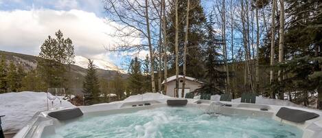 A hot tub surrounded by snow and trees, with a mountain in the background.