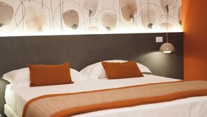 Habitación de hotel con cama, dos almohadas, cabecero, luz empotrada en la pared y una colcha.