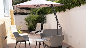 Un patio exterior con muebles modernos, incluyendo dos sillones y una mesa, bajo un gran paraguas.