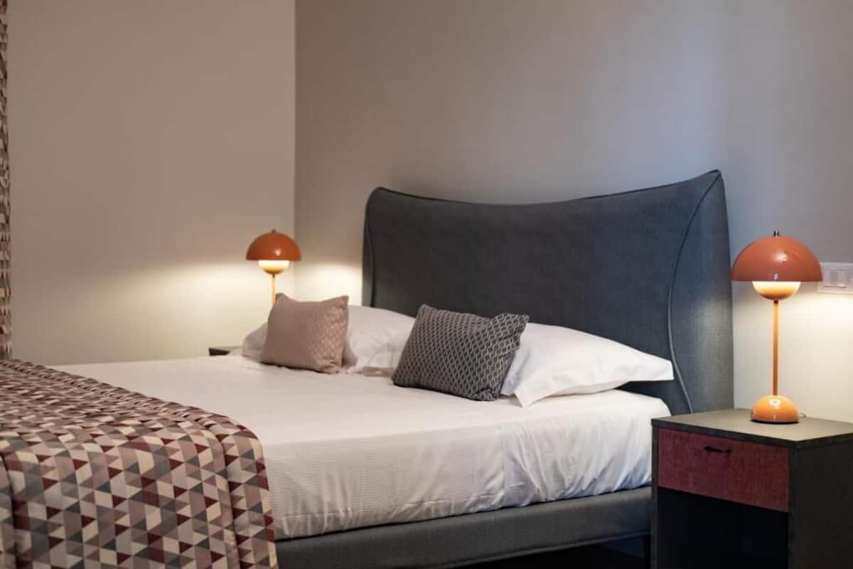 A neatly made bed with a geometric-patterned bedspread, a dark headboard, and two bedside lamps with orange shades.