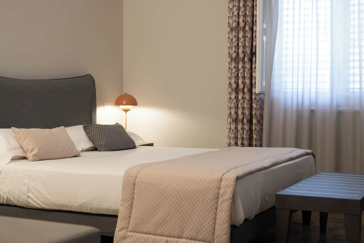 A neatly made bed with a patterned blanket, a bedside lamp, and a small table.