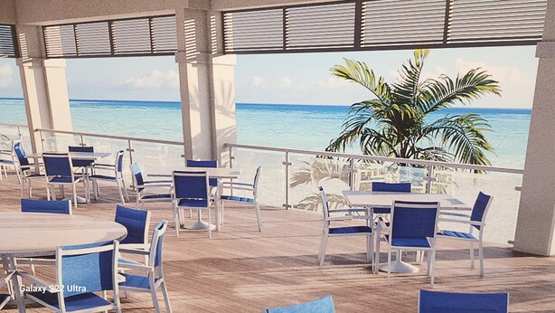 Un espace extérieur abrité, doté de tables et de chaises, offrant une vue sur une plage et l’océan.
