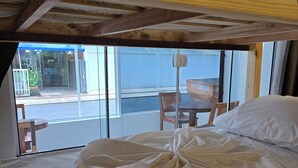 Una cama individual sobre otra, con un panel de control, una ventana que da a vistas exteriores, y una mesa y silla afuera.
