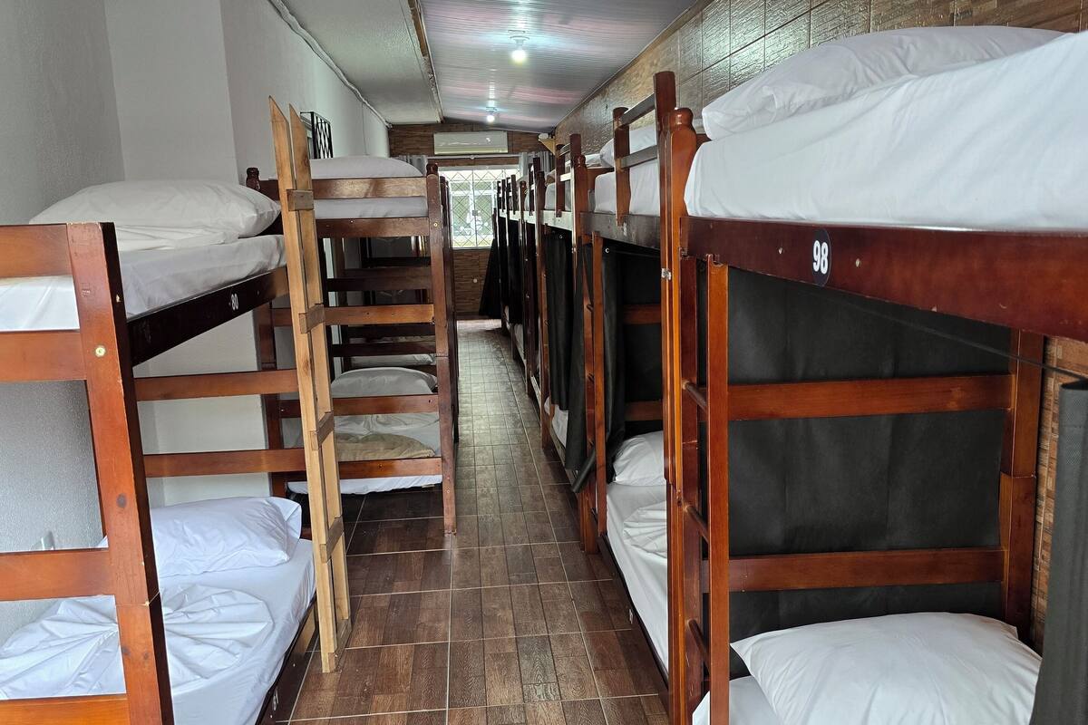 A dormitory room with bunk beds, wooden flooring, and a tiled ceiling.