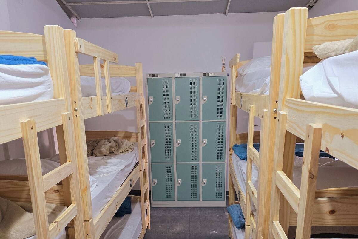 A narrow corridor with bunk beds on either side, leading to a set of green lockers.