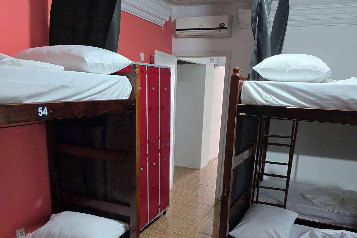 A dormitory room with bunk beds, numbered beds, a red storage unit, and an air conditioning unit on the wall.