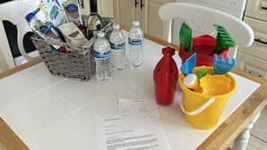 Une cuisine dotée d’un plan de travail en granit, de meubles blancs, d’une cuisinière et d’un lave-vaisselle. On trouve divers objets sur le plan de travail, notamment un panier, des bouteilles d’eau, un vaporisateur rouge et un seau jaune rempli de jouets.