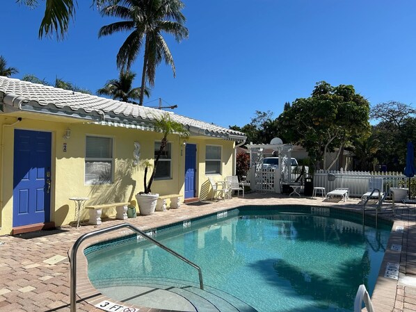 A pool area with a clear blue pool, a white fence, and a yellow building with blue doors.