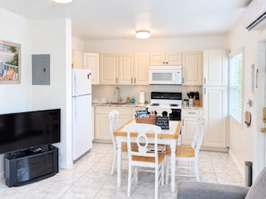 A compact kitchen with white cabinets, a microwave, a refrigerator, and a dining table with chairs.