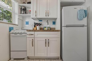Una cocina con armarios blancos, estufa, refrigerador y una ventana con persianas.