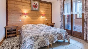 Une chambre à coucher avec une tête de lit en bois, un lit recouvert d’une couvre-lit à motifs de cœur, deux lampes de chevet et une fenêtre avec des rideaux.