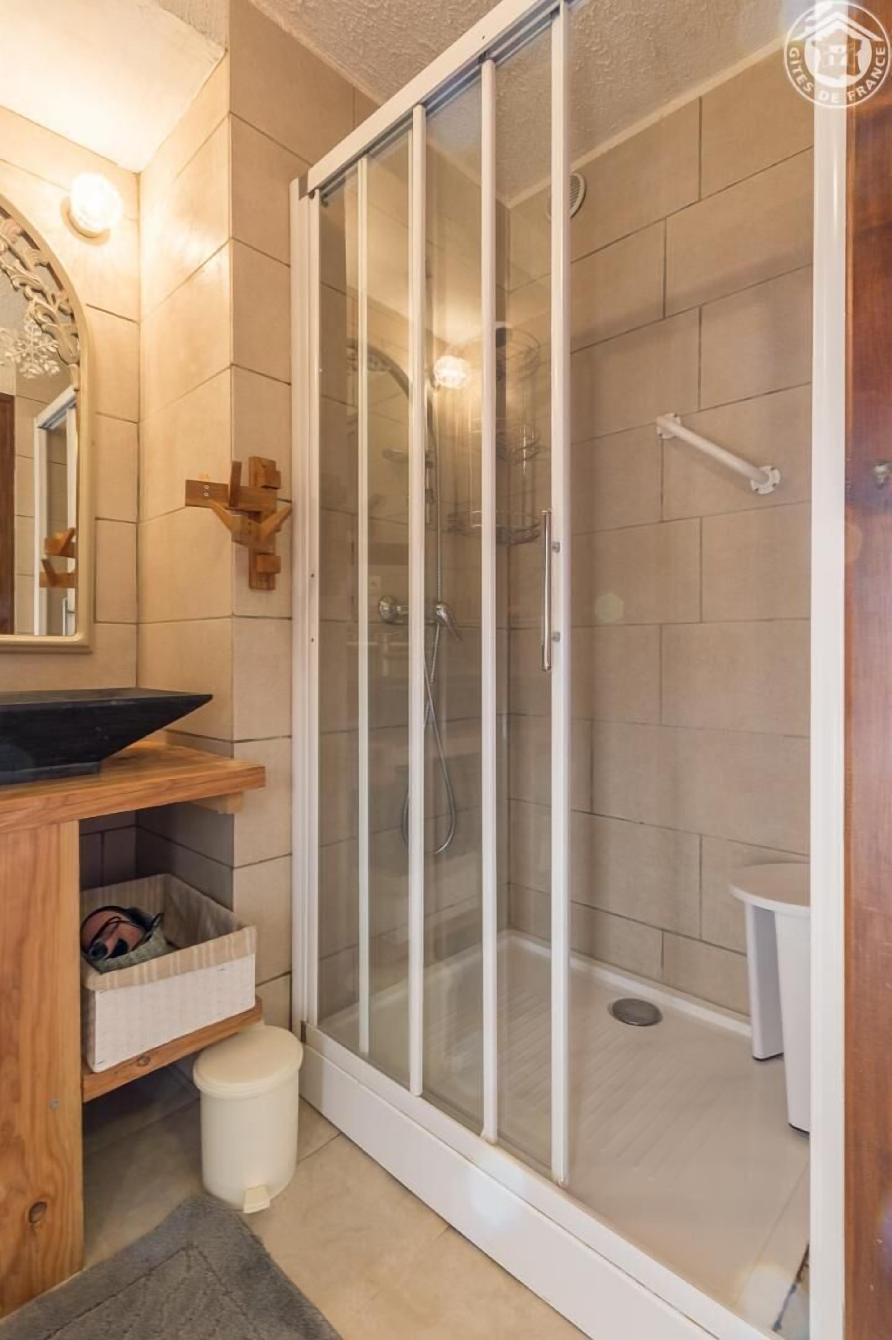 A bathroom with a glass-enclosed shower, a wooden vanity with a sink, and a mirror.