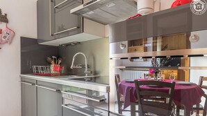 A modern kitchen with a built-in dishwasher, a stainless steel range hood, and a dining area with a table set for two. - PLEIN SOLEIL - BRIDES LES BAINS (BRIDES LES BAINS)