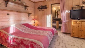 A wooden room with two beds, a television, and a bathroom visible through an open door. - PLEIN SOLEIL - BRIDES LES BAINS (BRIDES LES BAINS)
