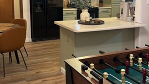 Una cucina moderna con isola centrale, zona pranzo con tavolo e sedie, e tavolo da calcio.
