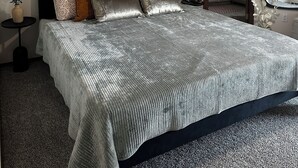 Una camera da letto con un letto, un quadro astratto appeso al muro, una ventola a soffitto e vista su una cucina attraverso una porta aperta.