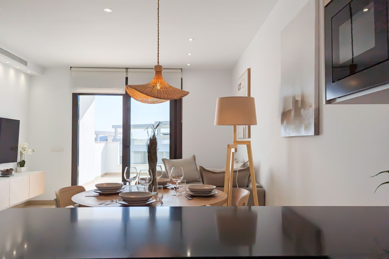 Un comedor moderno con una mesa redonda para cuatro personas, una lámpara colgante y un televisor montado en la pared.