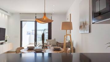Un comedor moderno con una mesa redonda para cuatro personas, una lámpara colgante y un televisor montado en la pared.