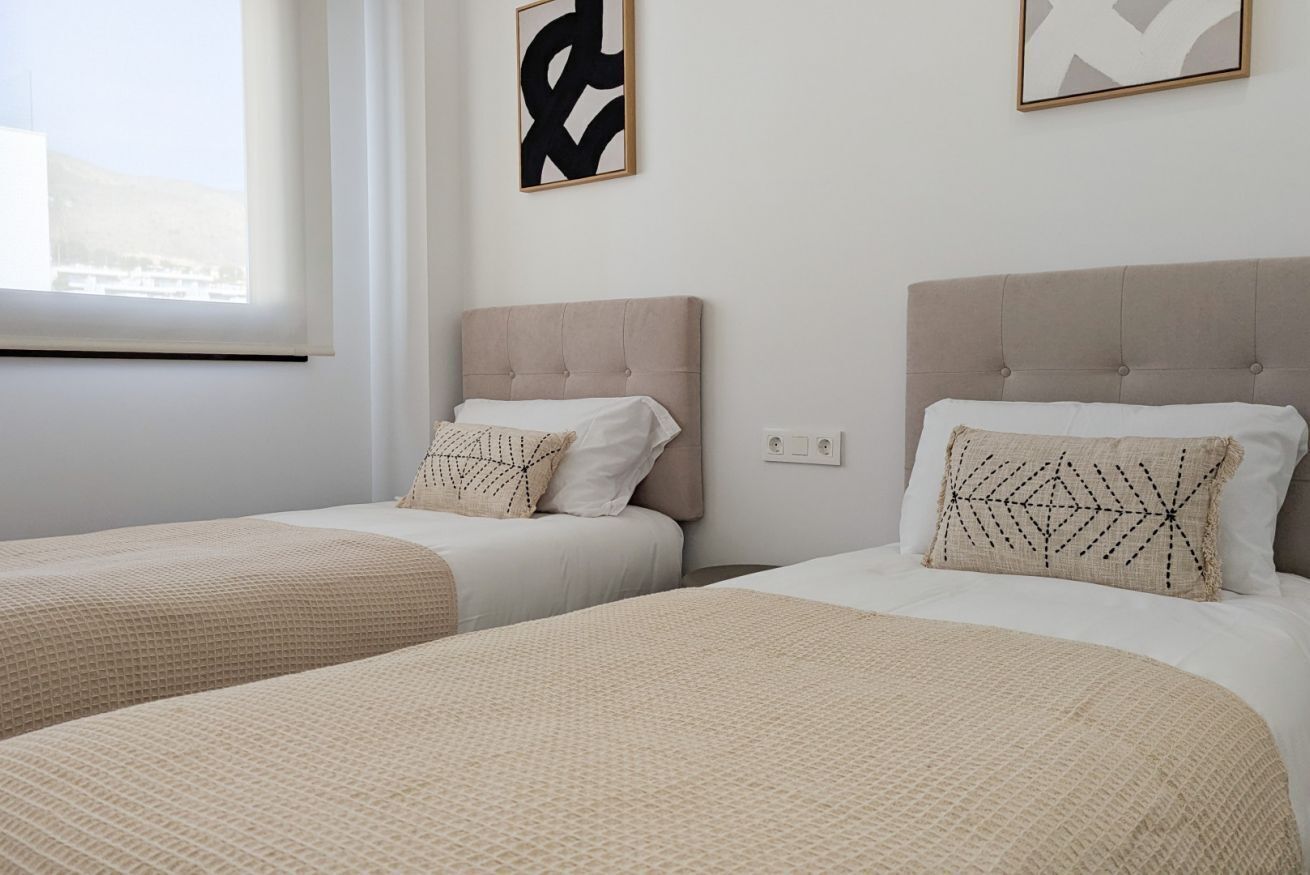 Two single beds with beige headboards and white bedding, a window with a view, and abstract art on the wall.
