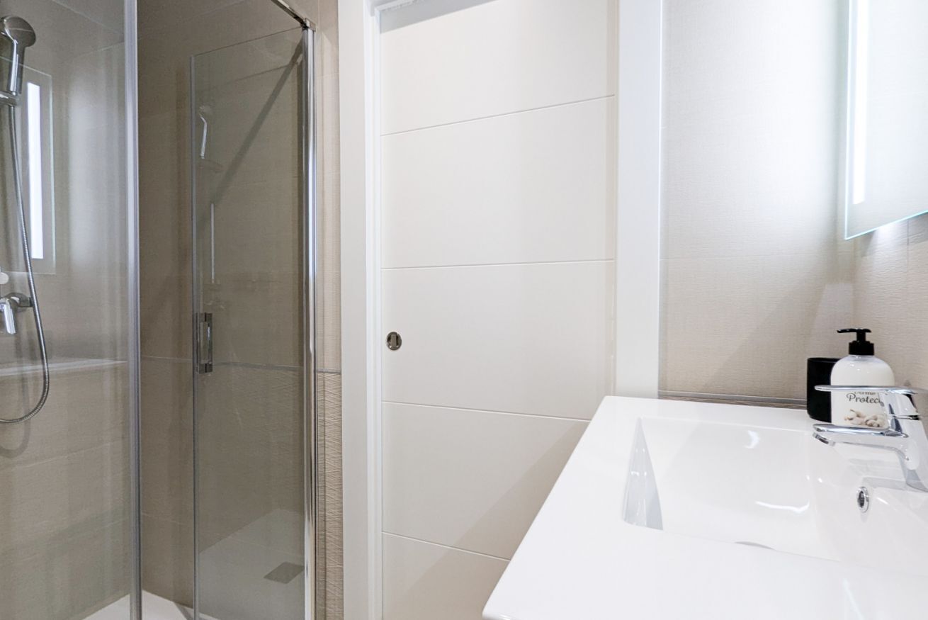 Un baño moderno con ducha de vidrio, lavamanos blanco y espejo.