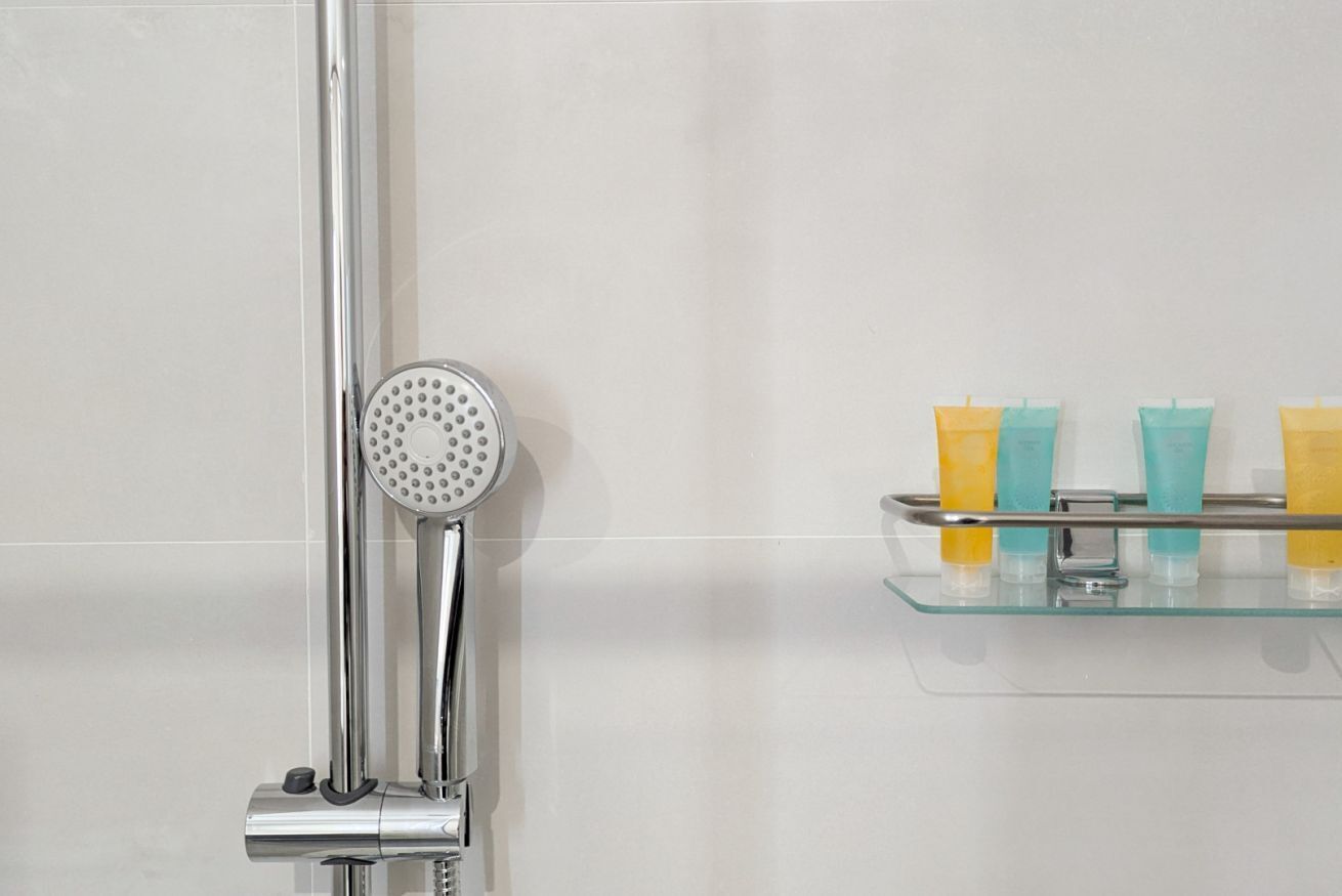 Een douche met een handdouche en een glazen plank met toiletartikelen.