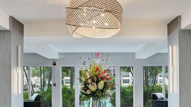 A modern lobby with a glass table, a decorative light fixture, and a view of greenery outside.