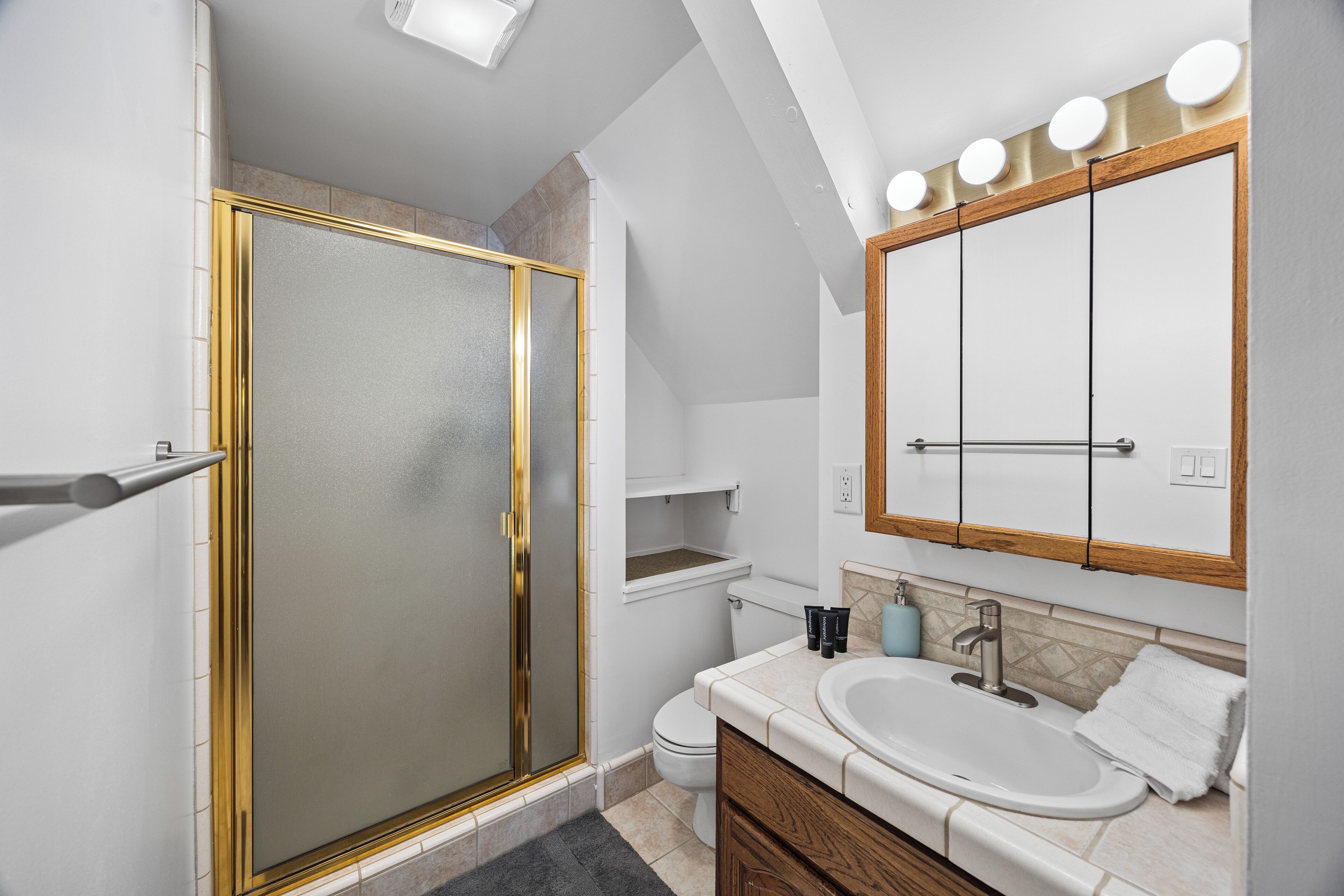 Un baño moderno con ducha de vidrio, tocador con lavamanos y un espejo grande con luces arriba.
