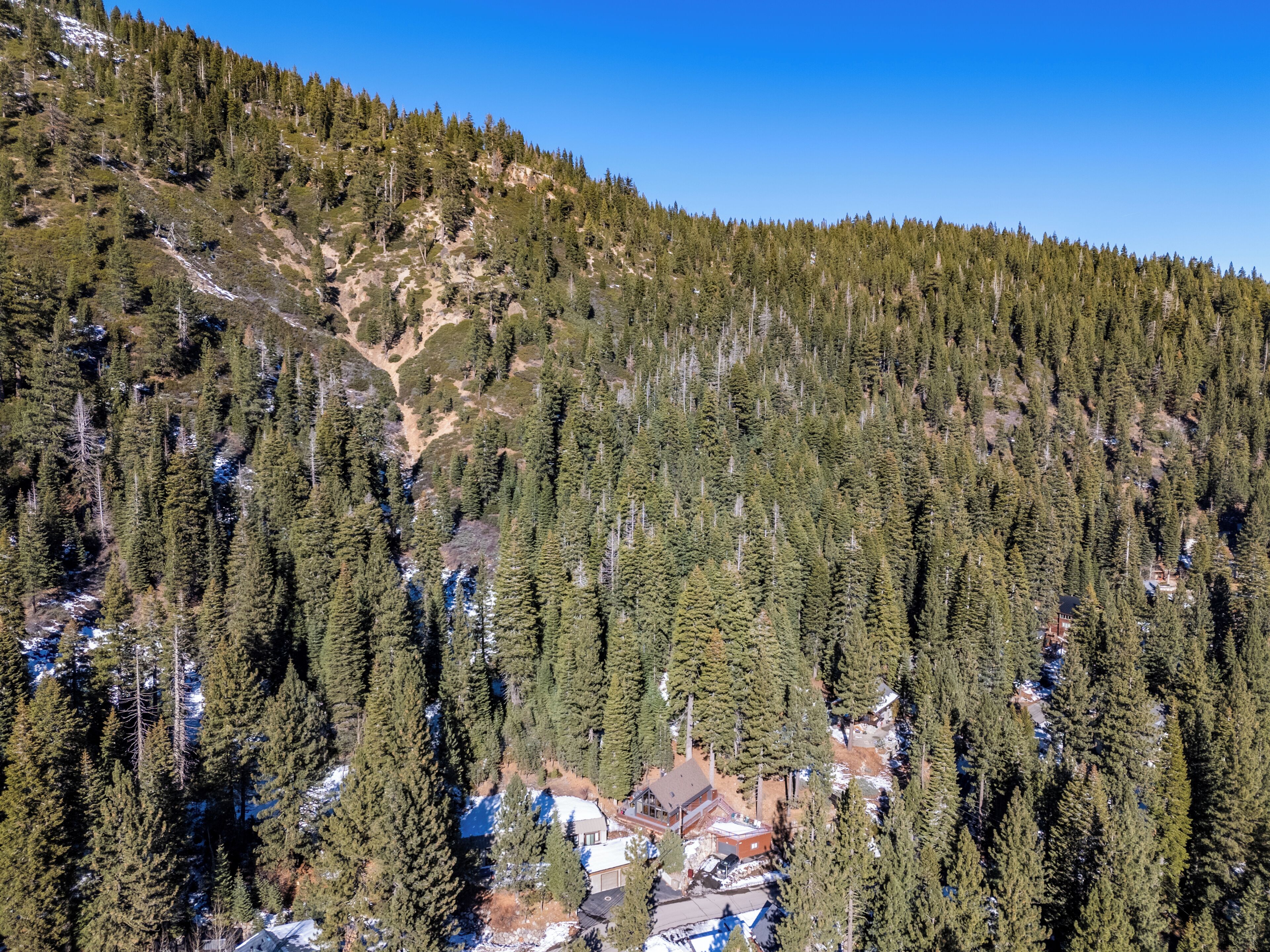 A mountainous area with dense coniferous forest and a small cluster of buildings at the base, likely a lodge or cabin.