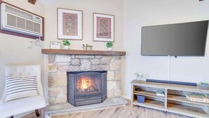 Una sala de estar con chimenea de piedra, un televisor de pantalla plana montado en la pared y un mueble de madera para entretenimiento.